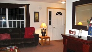 A living room with a dark-colored sofa, a small wooden side table with a lamp, a fireplace, and a door with a white frame. - Sunday River Rental (Bethel)