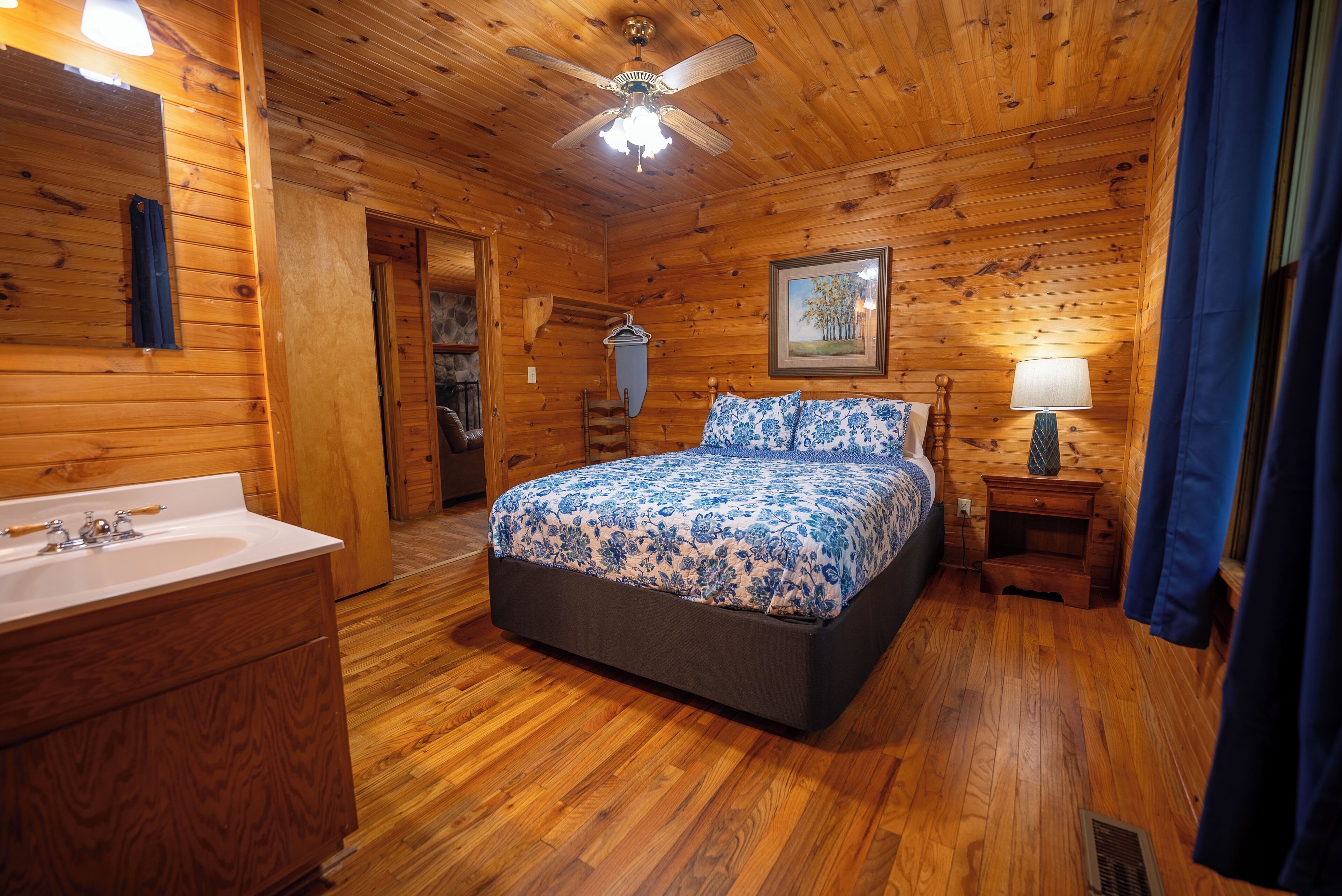 A wooden cabin bedroom with a bed, a nightstand, a lamp, a dresser, and a ceiling fan.