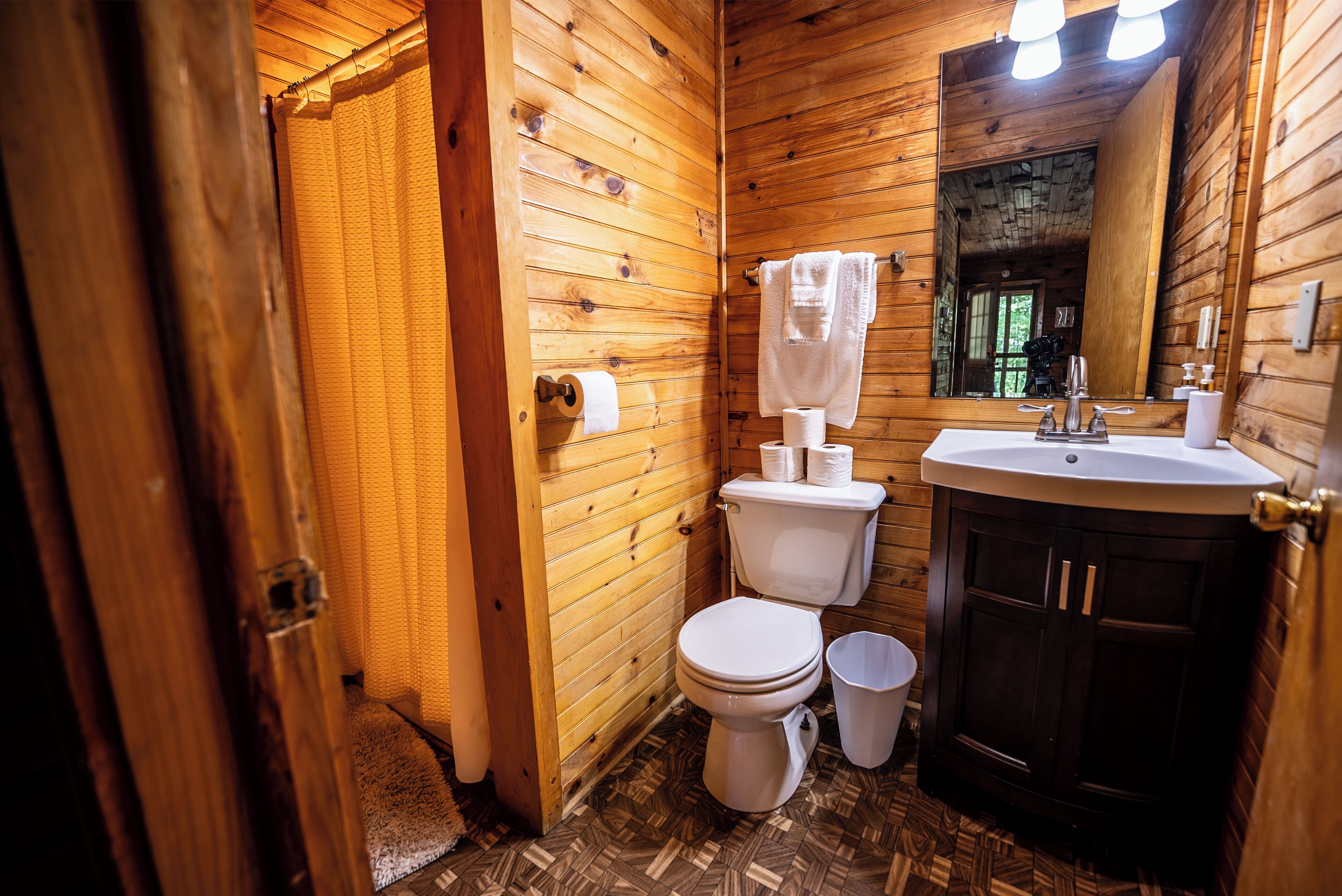 A wooden-paneled bathroom with a toilet, sink, and mirror.