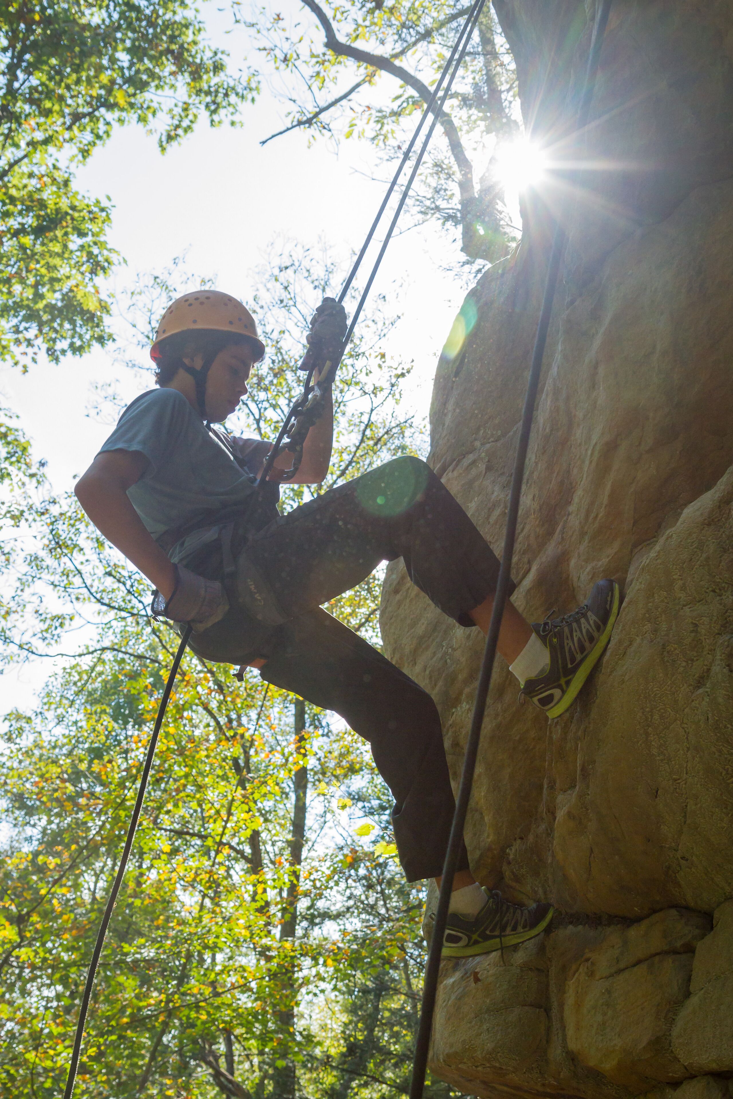 A person rock climbing a large rock face with safety ropes.
