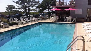 A swimming pool with white lounge chairs and umbrellas, surrounded by a fence and trees. - Direct Beachfront Condo With Great Ocean Views From Couch Or On The Porch (North Wildwood)