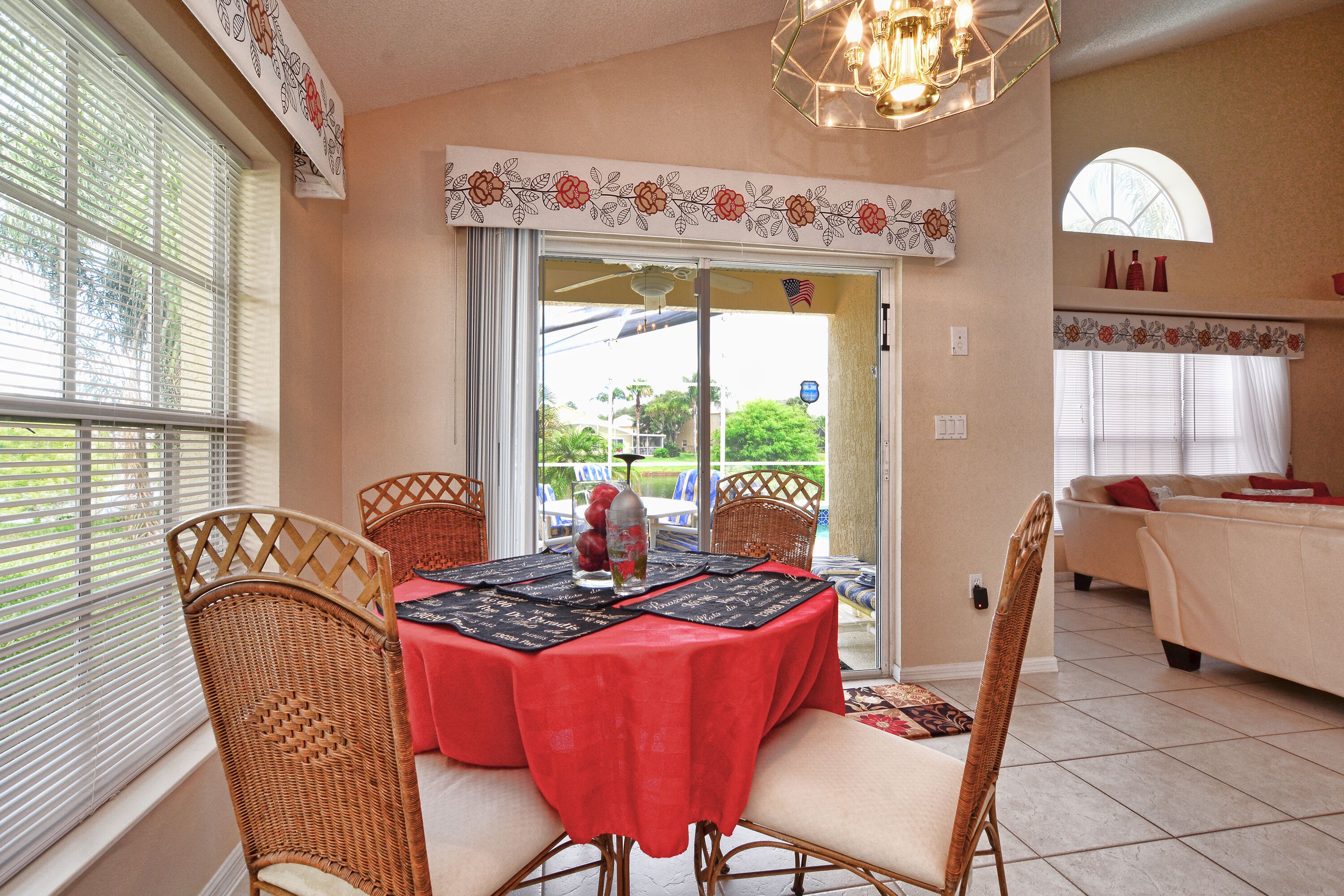 A dining area with wicker chairs, a red tablecloth, and a view through a glass door.