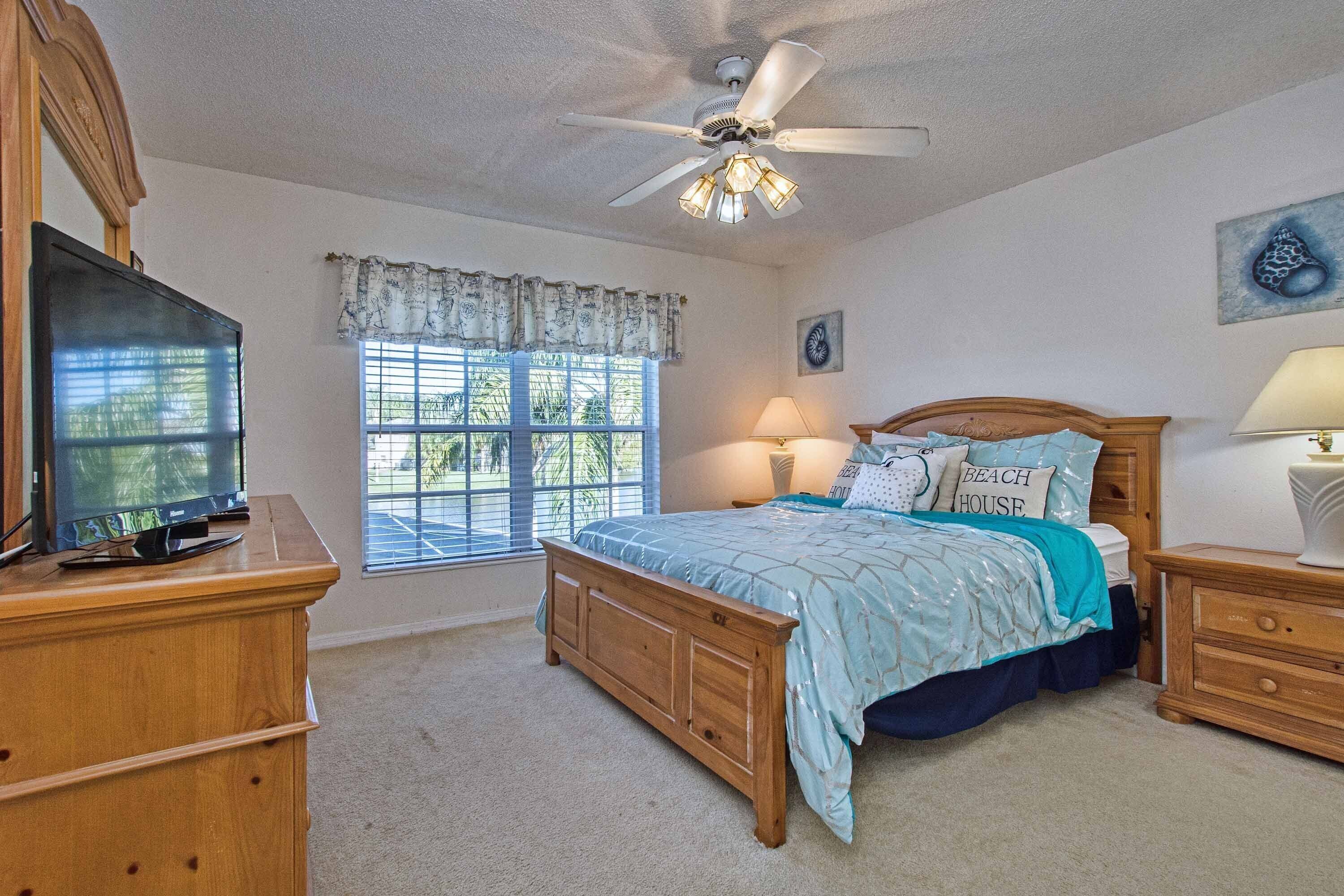 A bedroom with a bed, a television, a ceiling fan, and a window with blinds.