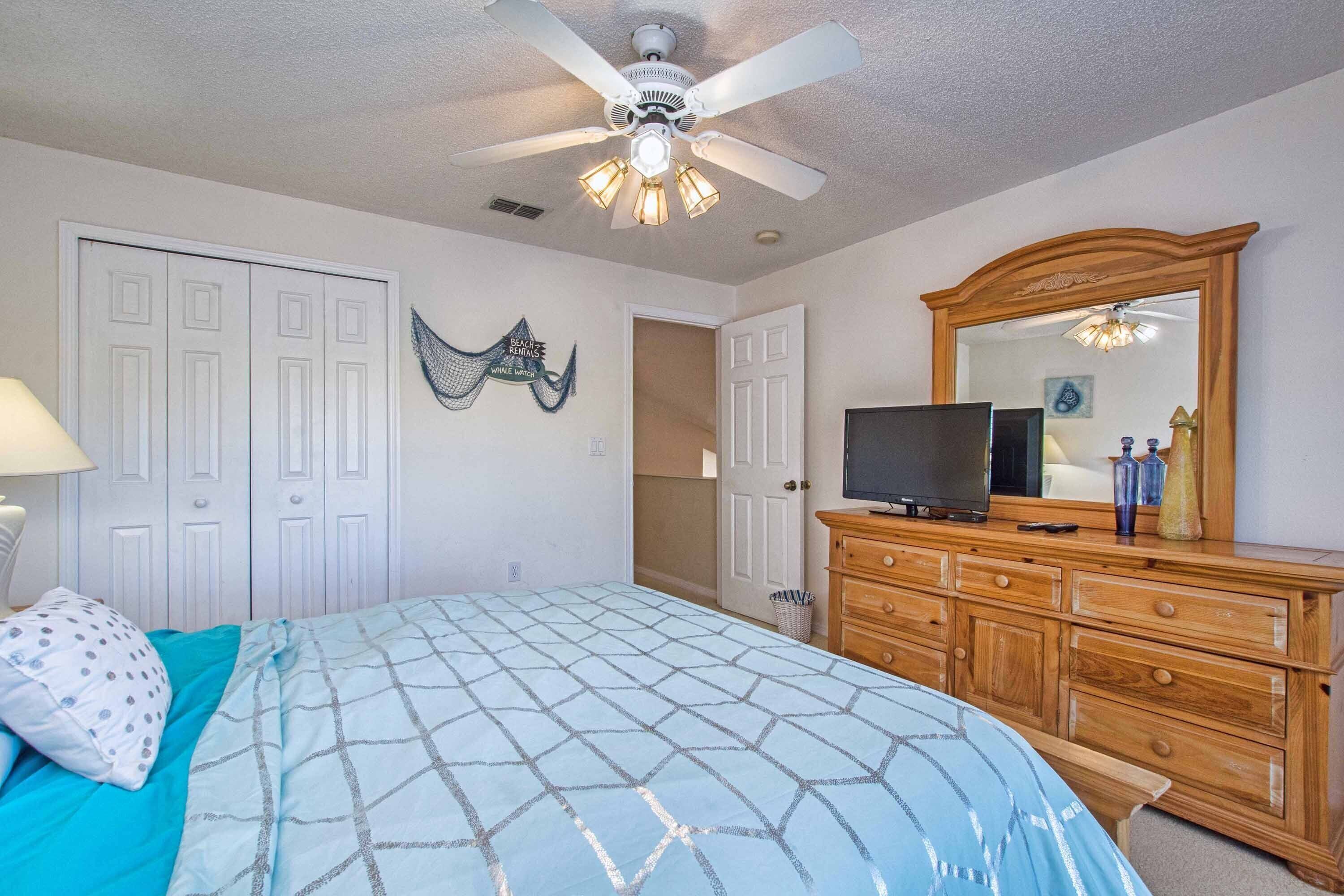 A bedroom with a bed, dresser, television, and ceiling fan.