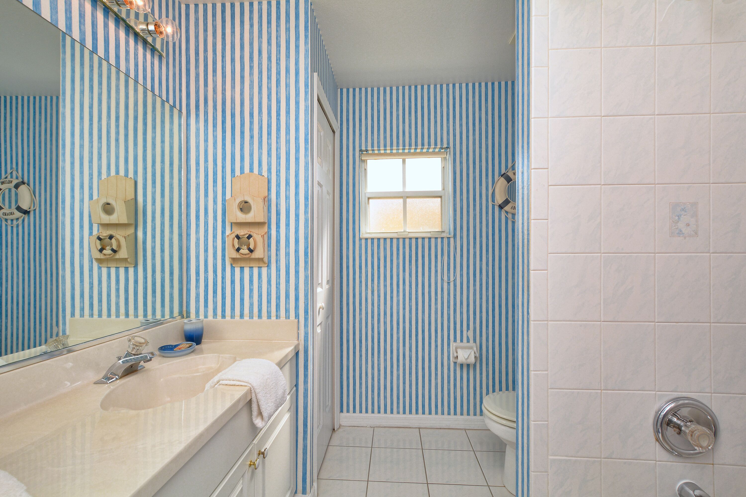 A bathroom with striped blue and white walls, a white sink with a mirror, and a shower area.