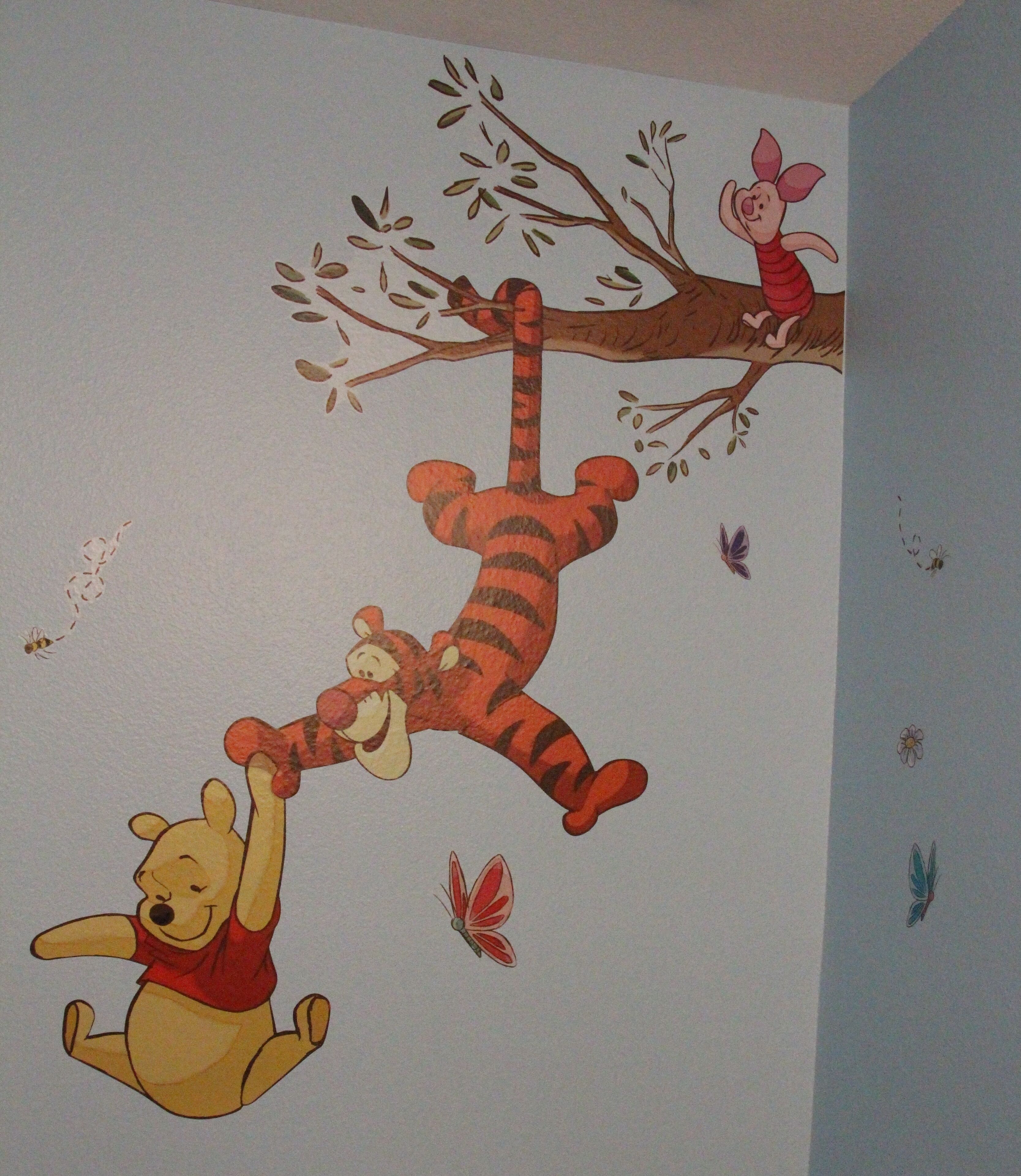 Eine Wand mit einem Wandbild von Winnie Puuh und Tigger, einem Ast und einem Schmetterling.
