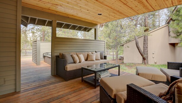 A covered outdoor seating area with a sofa and chairs, wooden flooring, and a view of the backyard. - 16 Yellow Pine - Gorgeous Golf Course, Covered Outdoor Living, Hot Tub, 3 King bedrooms, Bocce (Bend)
