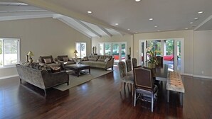 Ein geräumiges Wohnzimmer mit hoher Decke, großen Fenstern und einem Essbereich mit einer Bank und Stühlen.