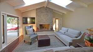 Ein Wohnzimmer mit Kamin aus Stein, einem großen Fernseher und einer Decke mit Dachfenstern.