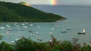 A coastal landscape with boats on calm waters, a lush green hill, and a rainbow in the sky. - Mesmerizing view with pool 2 bedroom stone cottage in Coral Bay (St John)