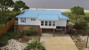 Ein zweistöckiges Haus mit blauem Metalldach, einer Holzterrasse und Blick auf den Strand.