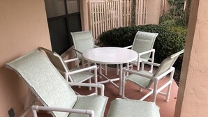 A patio with a round table and six chairs, surrounded by a beige wall and a wooden fence.
