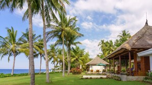 A tropical resort with a thatched-roof structure, palm trees, and a view of the ocean.