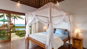 A bedroom with a wooden bed, white canopy, two bedside lamps, and a view of the pool and palm trees.