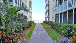 Un chemin menant à un bâtiment doté de balcons, entouré d’une végétation bien entretenue et offrant une vue sur la mer.