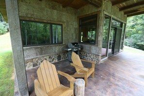 A covered outdoor area with Adirondack chairs, a grill, and a stone wall.