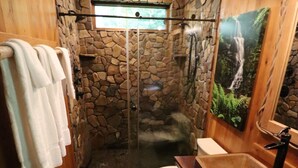 Un baño con pared de piedra, ducha, inodoro y lavabo.