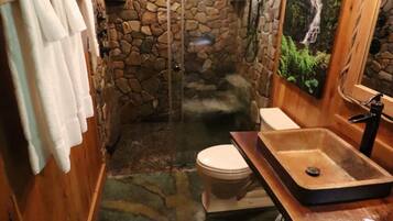A bathroom with a stone wall, a shower, a toilet, and a sink.