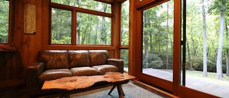 Una habitación con sofá de cuero, una mesa de centro de madera y amplias ventanas con vistas al bosque.