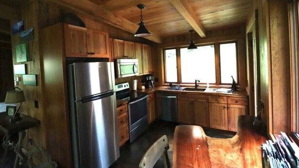 A wooden cabin interior with a kitchen featuring a refrigerator, microwave, stove, and sink.