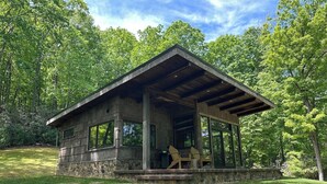 A stone cabin with a covered porch and two chairs.