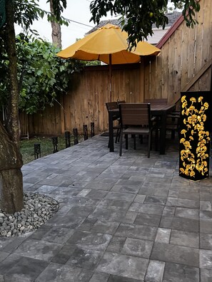 Eine Terrasse mit Steinplatten, einem Holzzaun und einem gelben Sonnenschirm.