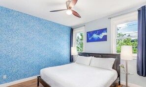 Ein Schlafzimmer mit einem Bett, einem Deckenventilator, einem Fenster mit Vorhängen und einem Wandbild.