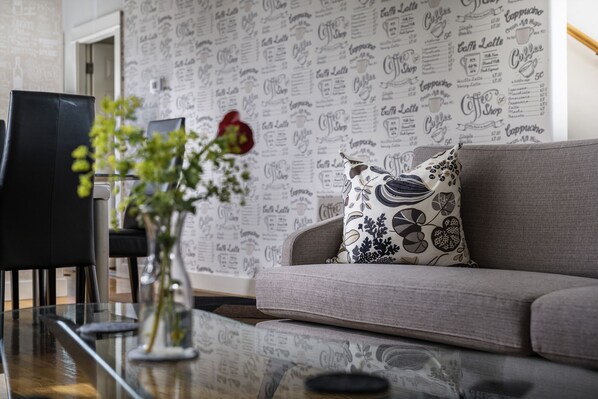 Ein modernes Wohnzimmer mit einem grauen Sofa, einem Zierkissen, einem Glastisch und einer Pflanze in einer Vase.