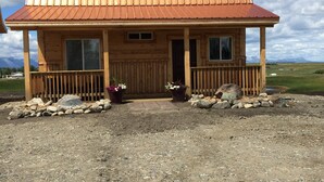Une cabane en bois avec un toit en métal, une véranda dotée de balustrades en bois et des plantes en pot devant l’entrée.
