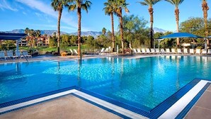 Une piscine entourée de chaises longues et de palmiers, le tout niché au cœur d’un paysage montagneux.