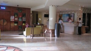 Eine Hotelhalle mit Empfangsschalter, Sitzgelegenheiten und einem großen Gemälde an der Wand.
