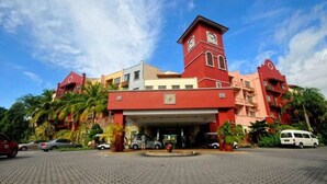 Ein Hotel mit einem zentralen rot gefärbten Gebäude, einem Glockenturm und einem überdachten Eingang.