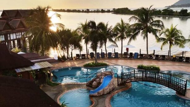Ein Swimmingpool mit Rutsche, Palmen und Blick auf das Wasser bei Sonnenuntergang.