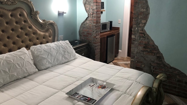 Un dormitorio con una cama grande, cabecera de madera, arco de ladrillo, una pequeña kitchenette y pared azul claro.