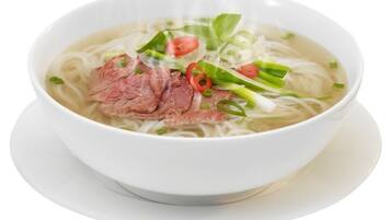 A bowl of noodle soup with beef slices, green onions, and red chili slices.
