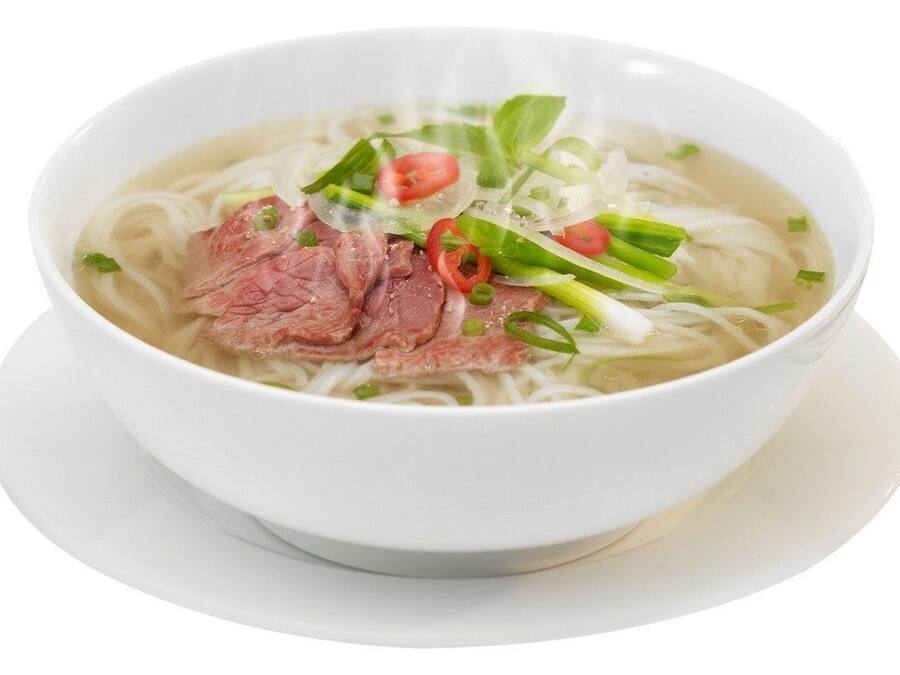 Un tazón de sopa de fideos con carne de res, cebolletas y rodajas de chile rojo.