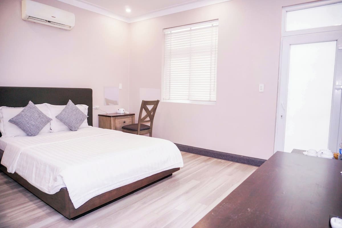 A bedroom with a bed, a chair, a nightstand, an air conditioner, and a window.