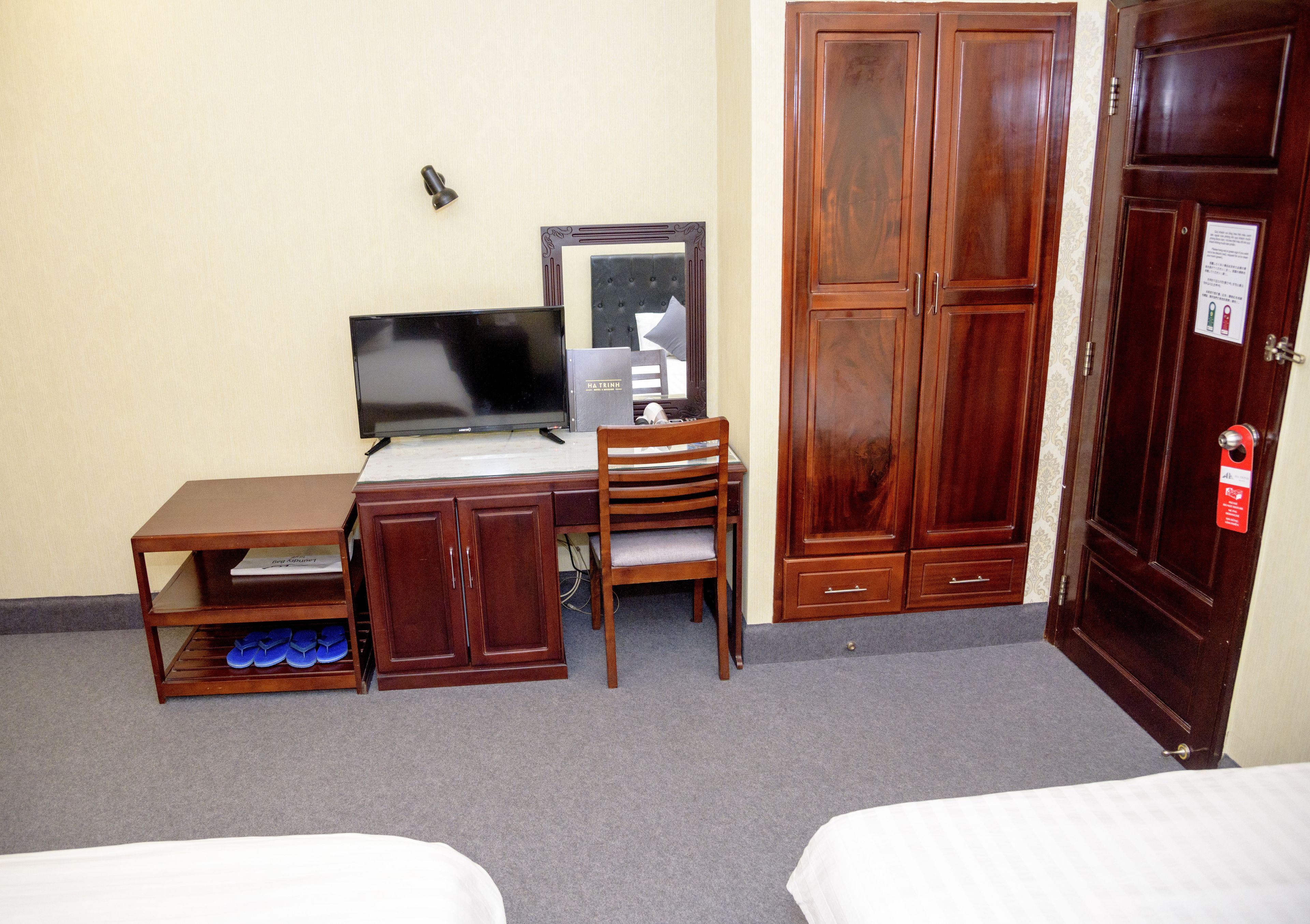 A hotel room with a wooden desk, a chair, a television, a wardrobe, and a bed.