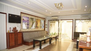 A spacious lobby with a large seating area, a flat-screen TV mounted on the wall, and a decorative wall with framed artwork.