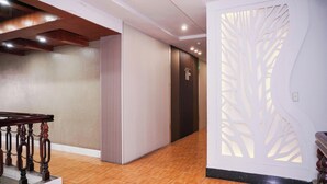 A hotel lobby with a wooden staircase, a reception desk, a wall with a decorative panel, and an elevator.