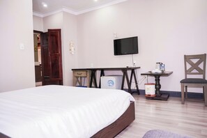 A hotel room with a bed, a desk with a television, a chair, and a small table with a trash bin. - Ha Trinh Hotel (Bien Hoa)