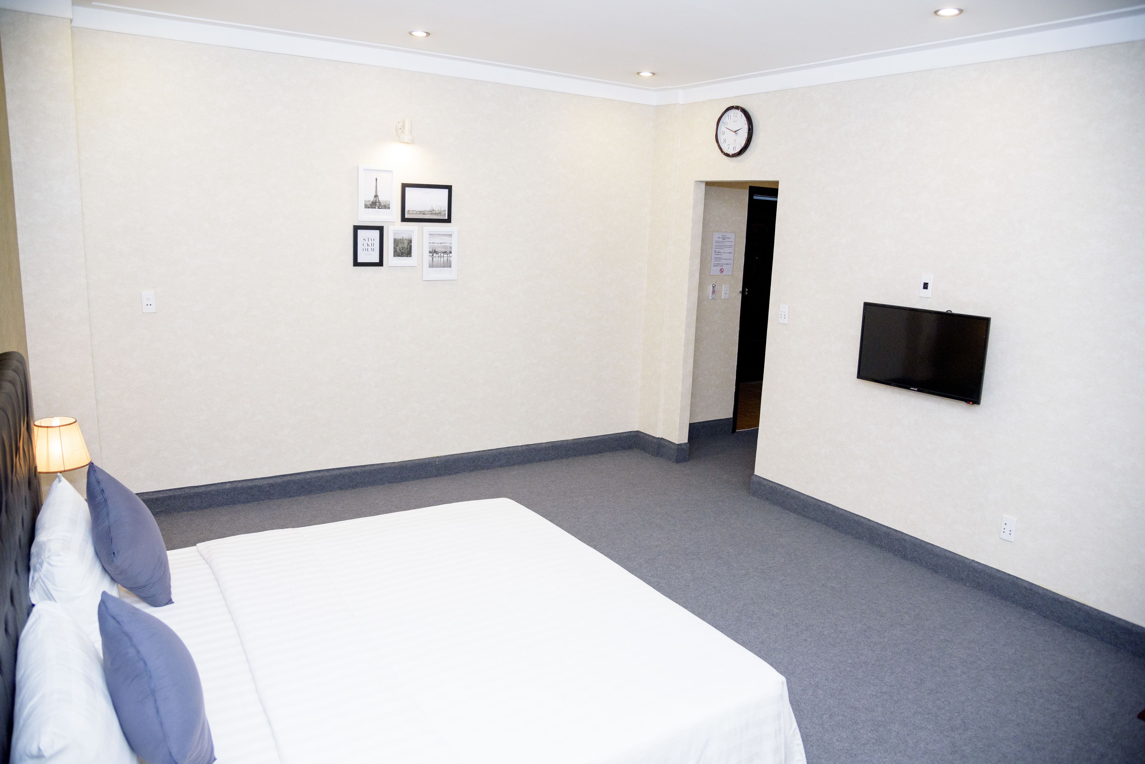 Hotellihuone, jossa on sänky, seinälle asennettu televisio ja kello.