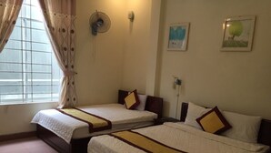 A hotel room with two single beds, a standing fan, a window with curtains, and a wall-mounted light. - Dang Tuan Hotel (Hue)