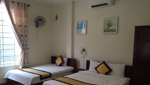 A hotel room with two single beds, a standing fan, an air conditioning unit, and a window with curtains. - Dang Tuan Hotel (Hue)