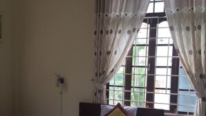 A single bed with a white and yellow bedspread, two pillows, a nightstand, and a window with curtains. - Dang Tuan Hotel (Hue)