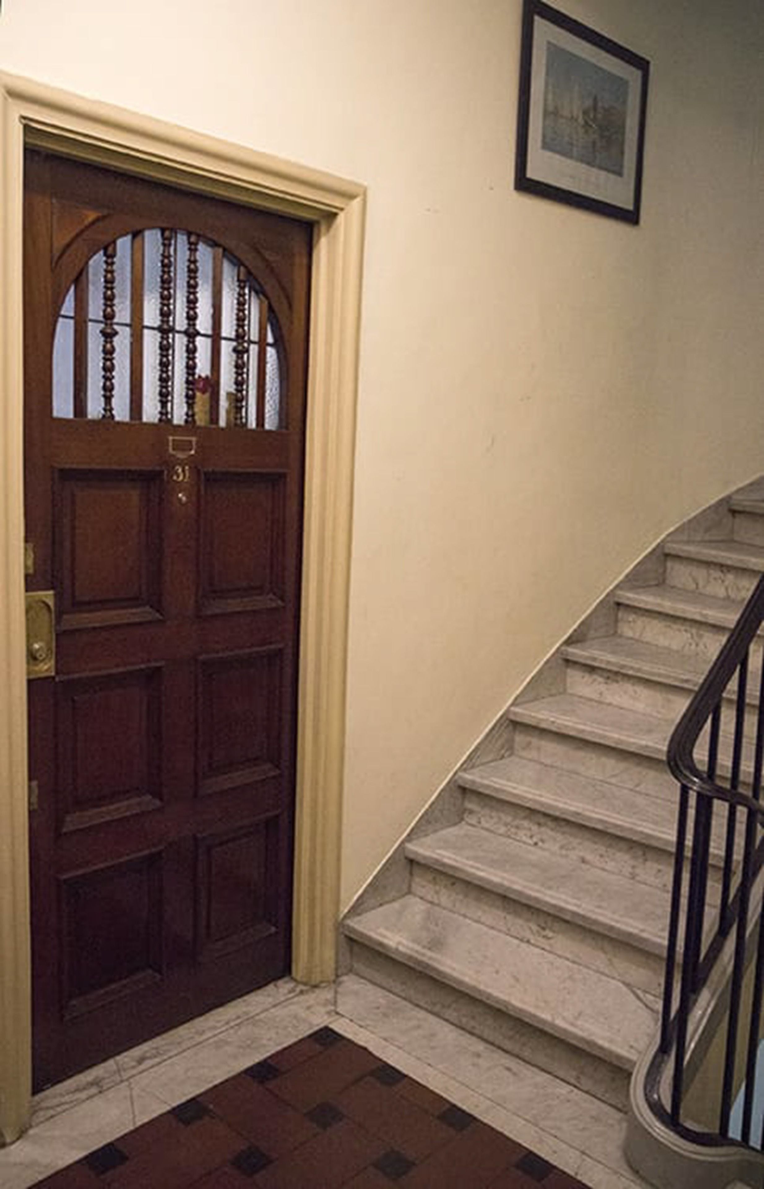 A wooden front door with a number plate, a staircase with a handrail, and a framed picture on the wall.