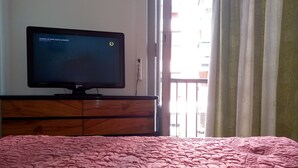 Una camera d'albergo con un letto, una televisione su un comò in legno e una finestra con tende.