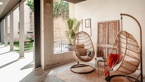 A room with two wicker hanging chairs, a small table, and a view of a garden through large windows. - Astuto Boutique Jerez - Adults Only (Jerez de la Frontera)