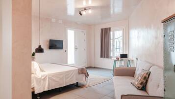A modern hotel room with a bed, a sofa, a TV, and a window with curtains.