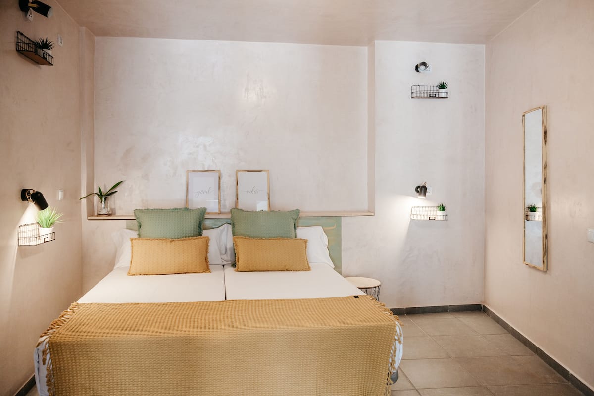 A bedroom with a bed, bedside tables, a mirror, and wall-mounted shelves with plants.